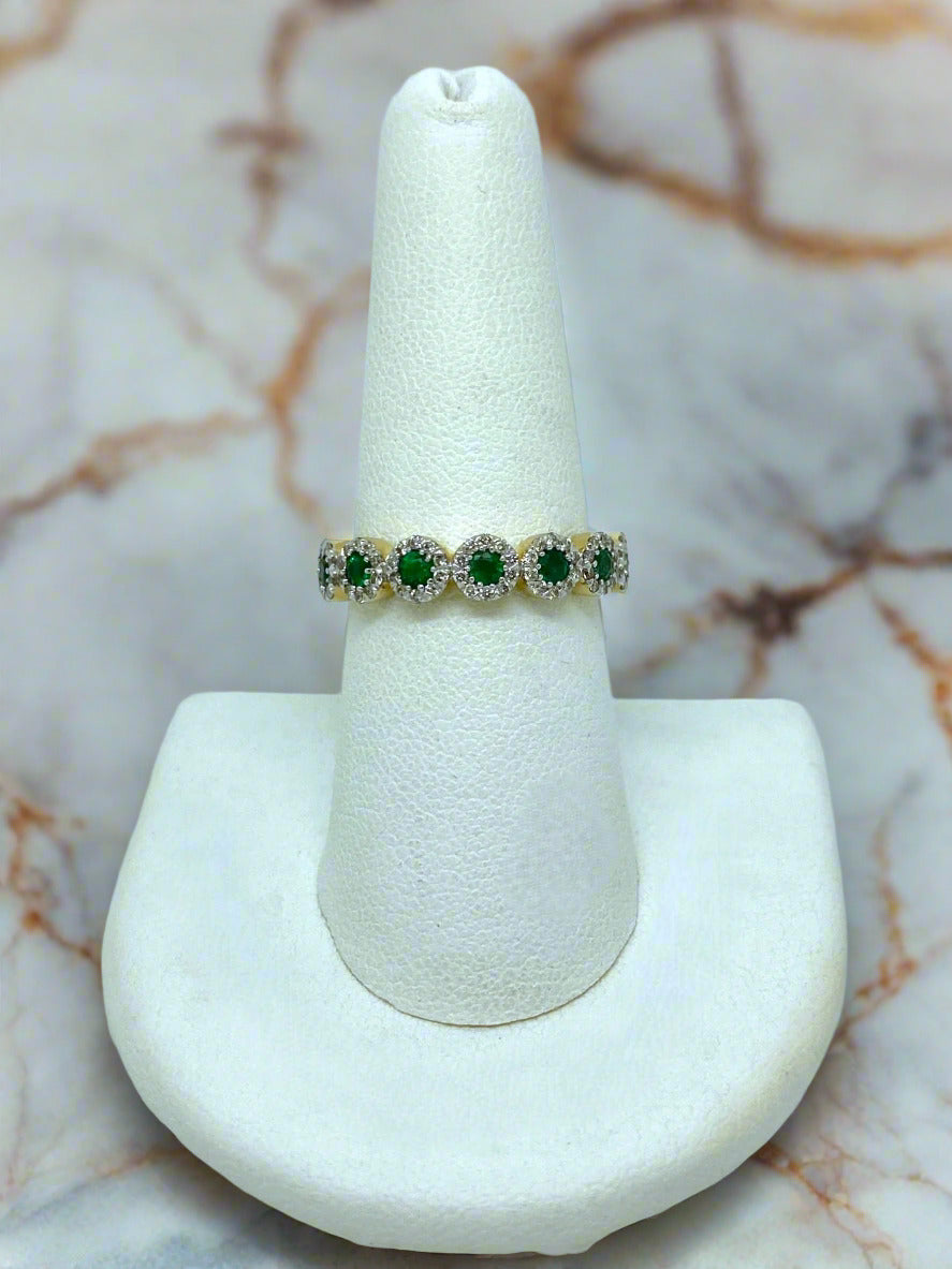 Ring with green and white gemstones on a white stand against a marble background