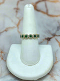 Ring with green and white gemstones on a white stand against a marble background