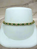 Bracelet with green and clear stones on a white stand