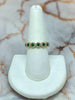 Ring with green and white gemstones on a white stand against a marble background