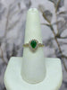 Gold ring with pear cut emerald center stone and diamond halo with diamond accents halfway down the band