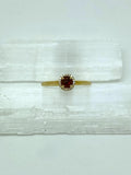 yellow gold ring with round garnet center stone in a halo of diamonds