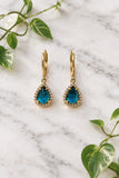 yellow gold dangle earrings with pear-shaped london blue topaz center stones, surrounded in halo of diamonds