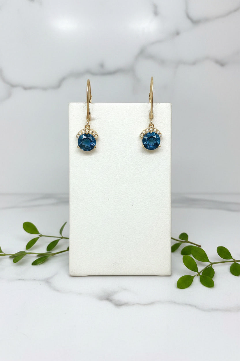 pair of yellow gold dangle earrings with blue topaz center stone and line of diamonds above