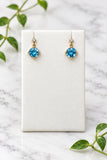 yellow gold dangle earrings with round swiss blue topaz center stones and a diamond accent on each