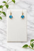 yellow gold dangle earrings with round swiss blue topaz center stones and a diamond accent on each