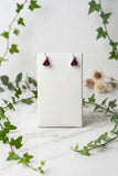 white gold stud earrings set each with a small diamond accent stone and each with a trillion cut rhodolite garnet