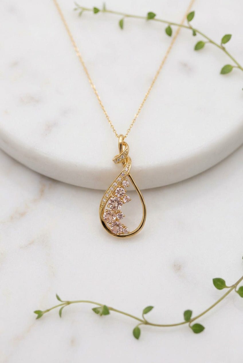 yellow gold chain and pendant, pendant is a teardrop with swirl on top set with morganite stones
