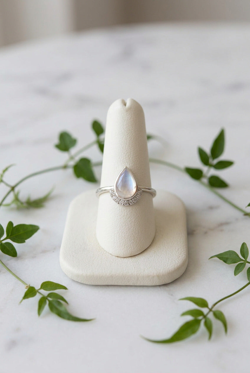 a white gold ring with a teardrop moonstone set in the center and teal sapphire accents stones